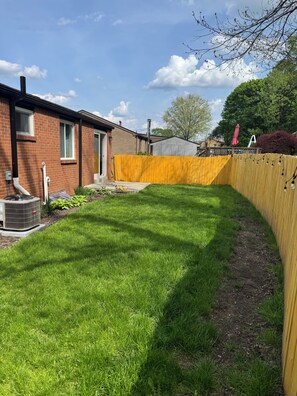 A backyard with a well-maintained lawn, a wooden fence, and a brick house.