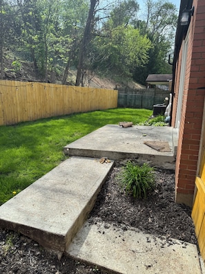 A backyard with a wooden fence, a concrete pathway, and a brick wall.