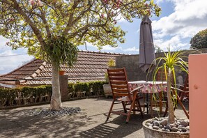 Un patio al aire libre con una mesa y sillas, rodeado de plantas en macetas y un árbol con flores rosas.