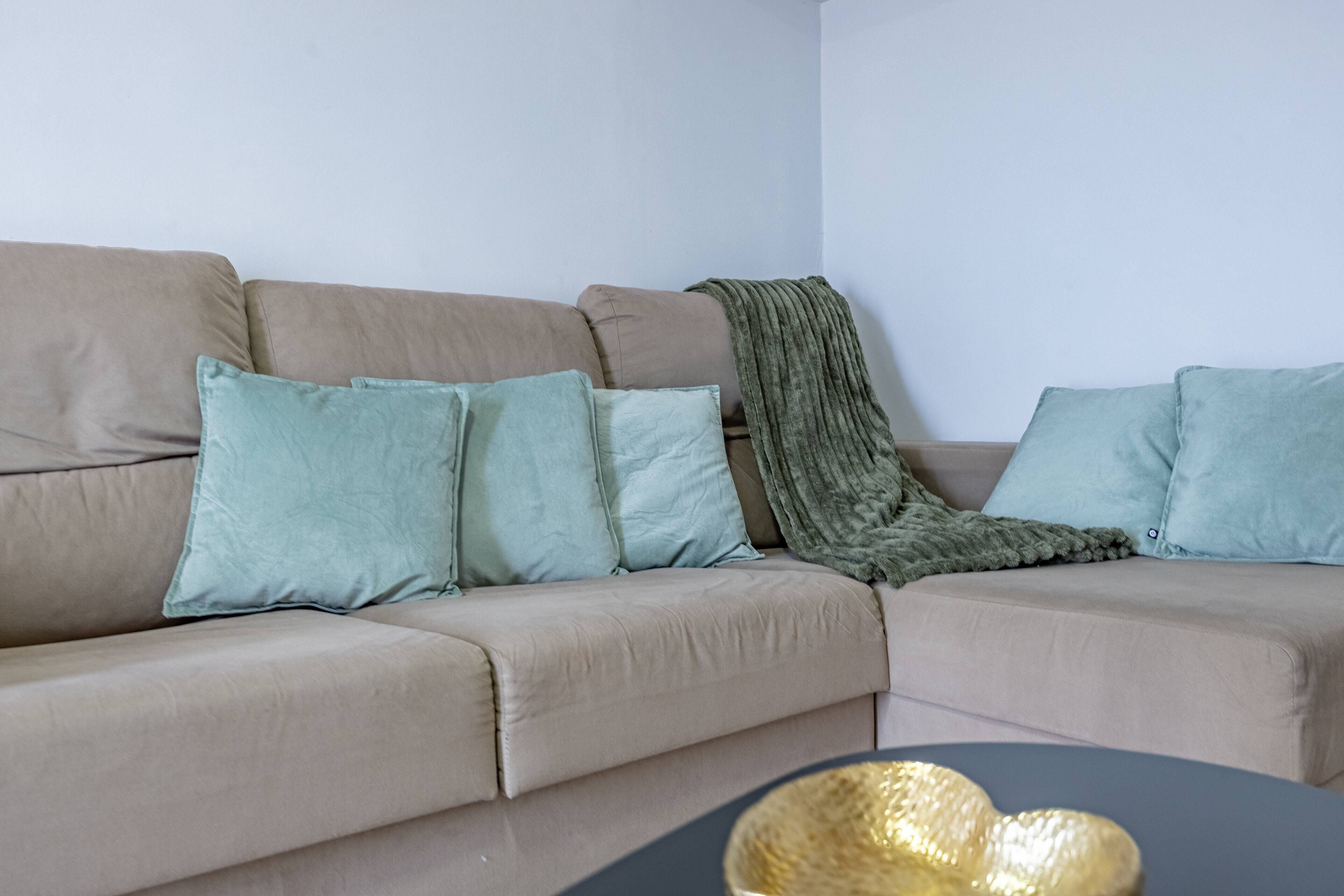 A beige sofa with light blue cushions and a green throw blanket.