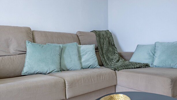 Ein beiges Sofa mit hellblauen Kissen und einer grünen Decke.