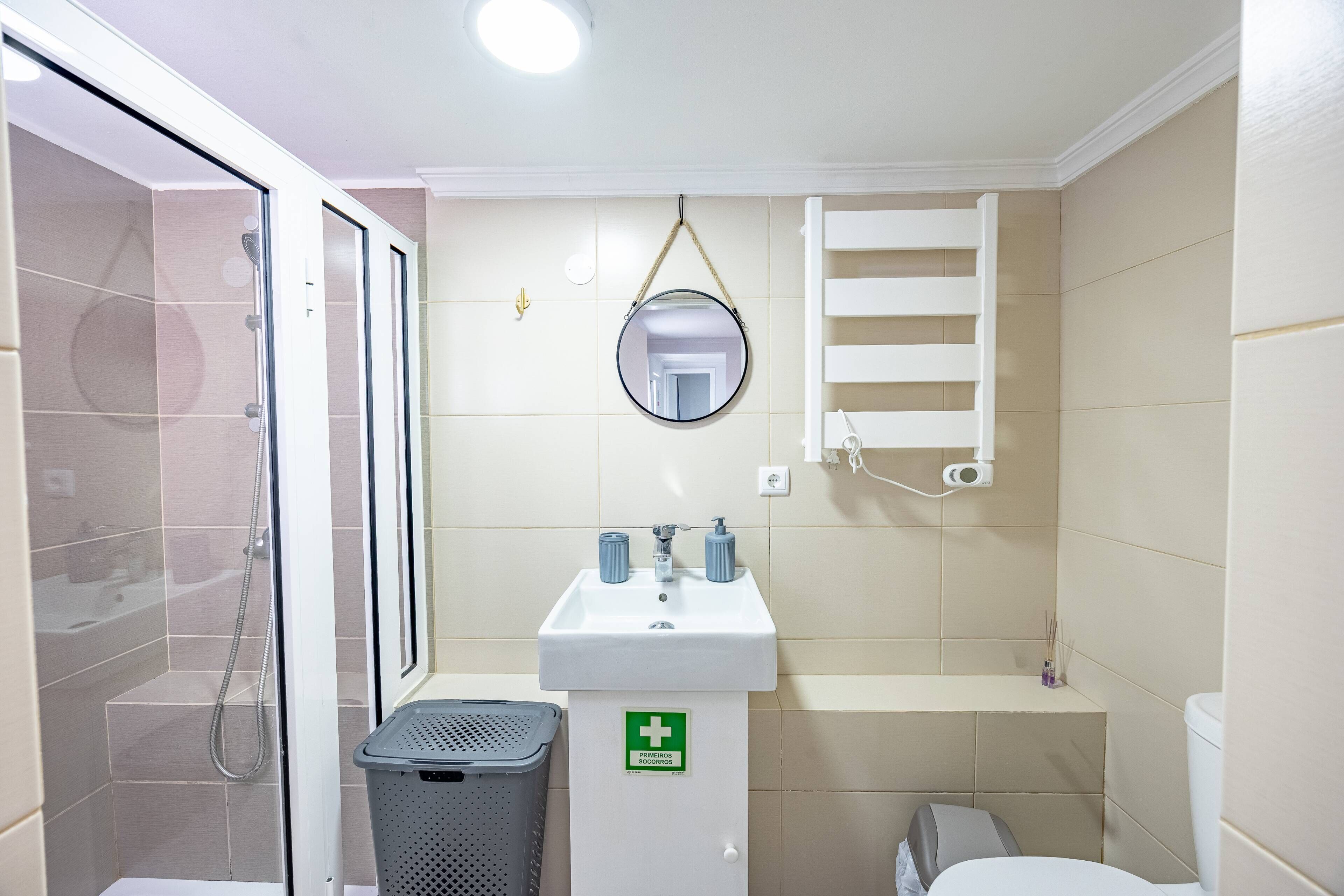 Une salle de bain avec une douche, un lavabo avec un miroir, des toilettes et une poubelle.