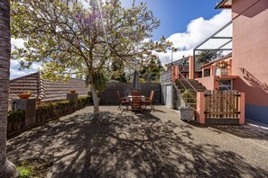 Une cour avec une table et des chaises, une porte en bois et un bâtiment à la façade rouge.