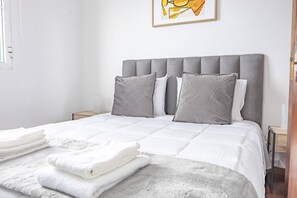 Un lit bien fait, avec une tête de lit grise, une literie blanche et des oreillers gris.