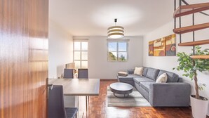 Een moderne woonkamer met een eethoek, houten vloeren, een grijze bank en een trap.