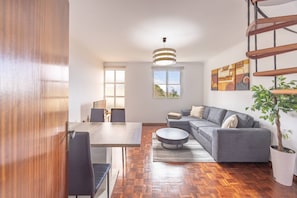 Ein modernes Wohnzimmer mit Essbereich, Holzboden, einem grauen Sofa und einer Treppe.