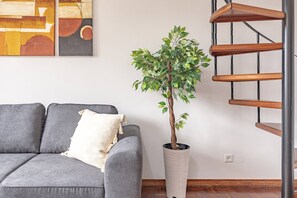 Um sofá cinzento com uma almofada, um vaso de planta e uma escada espiral de metal.