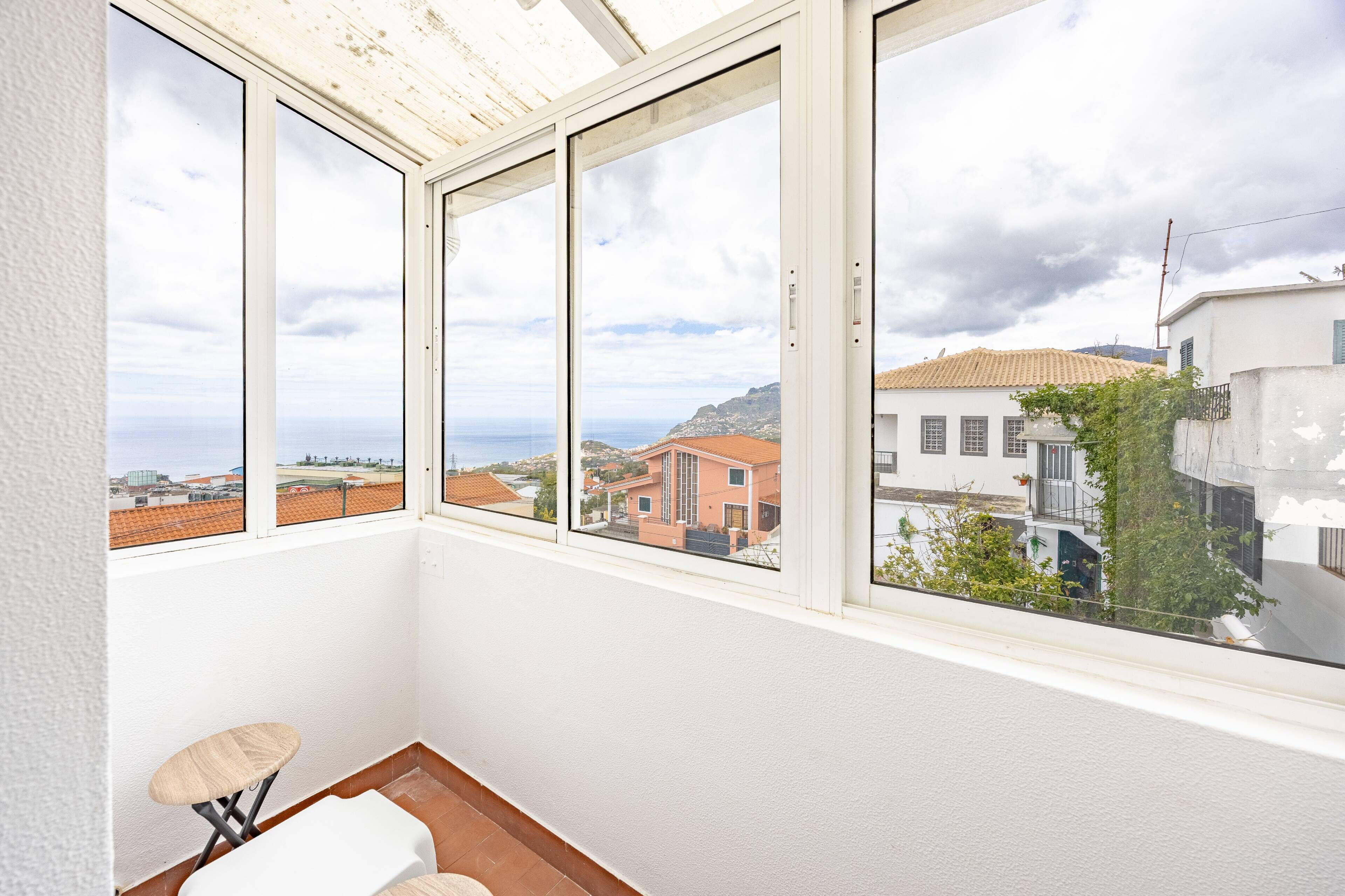 Ein Zimmer mit Blick auf eine Küstenstadt, ein kleiner Hocker und ein weißer Stuhl.