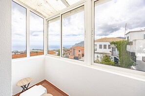 Um quarto com vista para uma cidade costeira, um banquinho pequeno e uma cadeira branca.