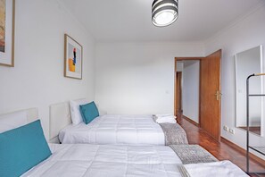 Ein Hotelzimmer mit zwei Betten, einem Bild an der Wand, Holzboden und einer Tür zu einem weiteren Raum.