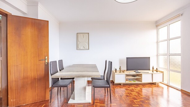 Een moderne woonkamer met een houten eettafel, zwarte stoelen, een flatscreen televisie en een groot raam.