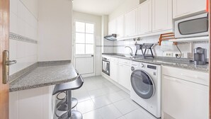 Een compacte keuken met witte kastjes, een ingebouwde oven, een wasmachine en een magnetron.