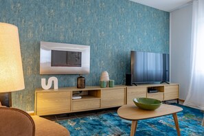 A modern living room with a blue textured wall, a flat-screen TV, a wooden cabinet, a green bowl, and a lamp. - Cozy Haven Santana by YOUR KEY (Santana)