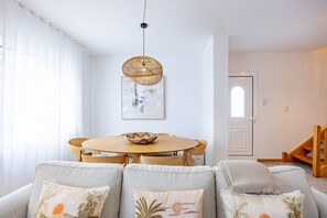 A modern living room with a round wooden table, grey upholstered sofas, and a woven pendant light. - Cozy Haven Santana by YOUR KEY (Santana)