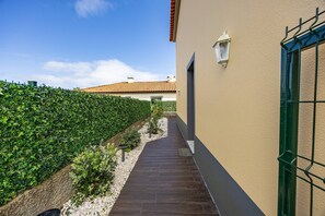 Ein Weg führt zu einem Gebäude mit einem Ziegeldach, umgeben von einer Hecke und einer Schotterfläche.