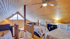 A cozy attic bedroom with wooden walls, a sloped ceiling, and a ceiling fan. There are two beds with matching headboards and a small desk with a lamp. - Wonderful 6-bedroom house with Hot Tub in charming Luray (Luray)