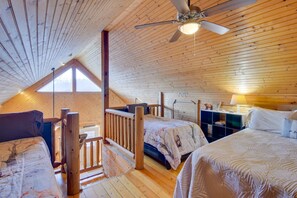 A cozy attic bedroom with wooden walls, a sloped ceiling, and a ceiling fan. There are two beds with matching headboards and a small desk with a lamp. - Wonderful 6-bedroom house with Hot Tub in charming Luray (Luray)