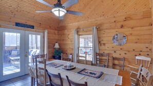A wooden cabin interior with a dining table, chairs, a ceiling fan, and a view through the glass doors. - Wonderful 6-bedroom house with Hot Tub in charming Luray (Luray)