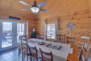 A wooden cabin interior with a dining table, chairs, a ceiling fan, and a view through the glass doors. - Wonderful 6-bedroom house with Hot Tub in charming Luray (Luray)