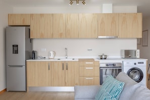 A compact kitchen with wooden cabinets, a built-in refrigerator, a sink, a kettle, a microwave, and a washing machine. - Endless Horizon by YOUR KEY (Santa Cruz)
