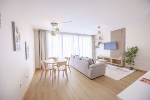 A modern living room with a sofa, dining table, and chairs. There is a TV mounted on the wall, a plant, and a window with curtains. - Endless Horizon by YOUR KEY (Santa Cruz)