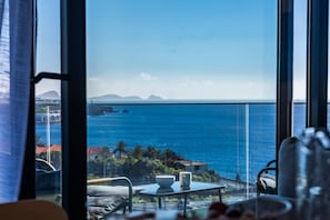 A room with a large window overlooking a coastal view, a table with a bowl and mug, and a chair. - Endless Horizon by YOUR KEY (Santa Cruz)