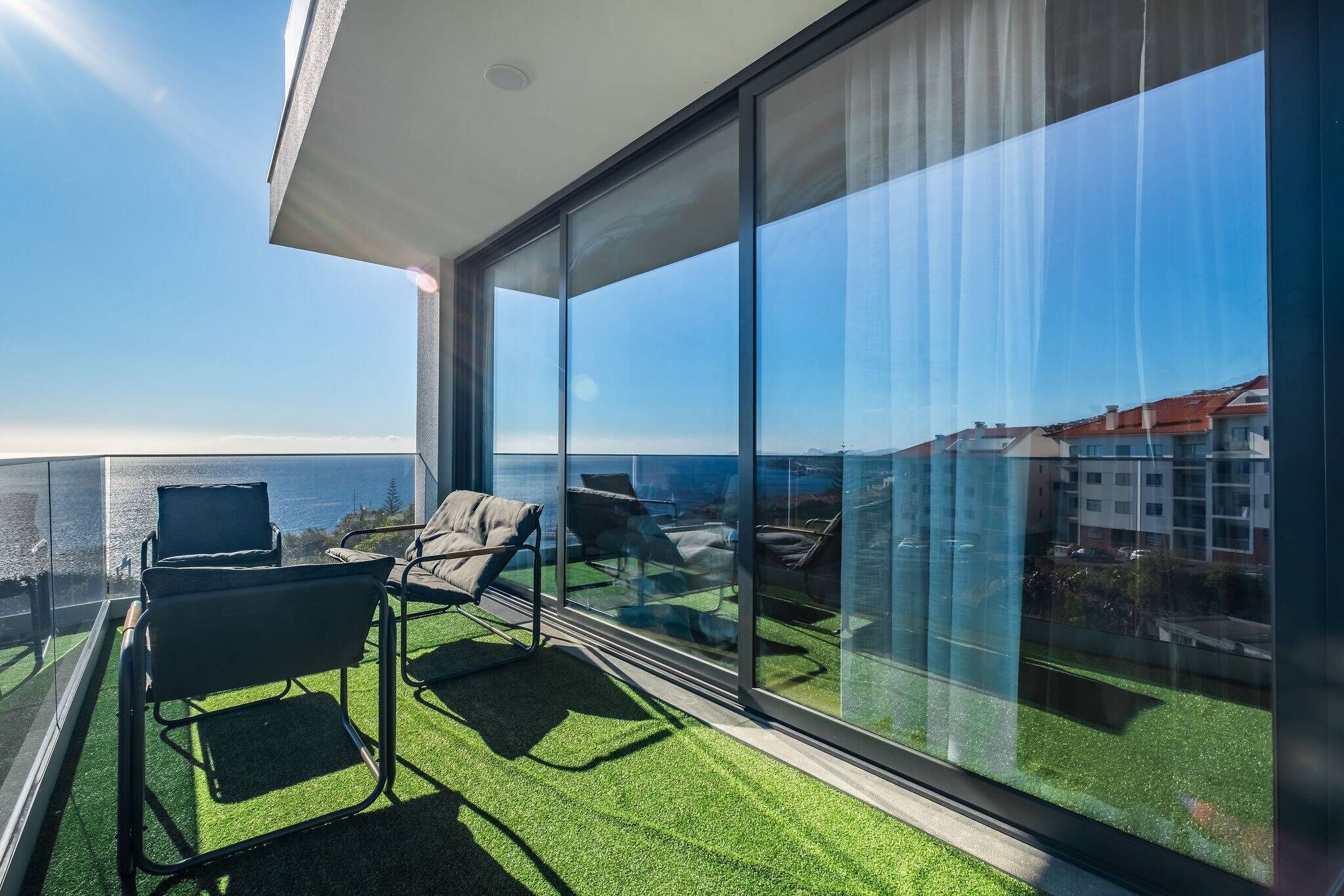 A balcony with two lounge chairs and a glass wall offering a view of the sea and buildings.