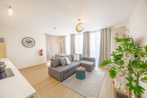 A modern living room with a grey sectional sofa, a small round coffee table, and a large window with curtains. - Fénix Horizon Suite by YOUR KEY (Santa Cruz)