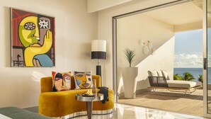 A modern living room with a yellow sofa, a round table, and a large window overlooking a balcony.