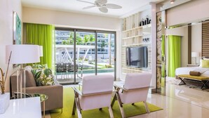 Een moderne woonkamer met een bank, stoelen, een televisie en een balkon met uitzicht op gebouwen en groen.