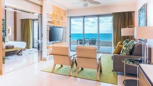 A modern hotel room with a balcony, a flat-screen TV, a sofa, and a dining area.