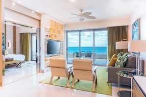 A modern hotel room with a balcony, a flat-screen TV, a sofa, and a dining area.