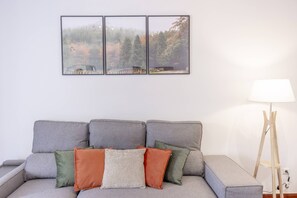 A grey sofa with three cushions in different colors, a floor lamp, and a framed picture on the wall. - Funchal Haven by YOUR KEY (Funchal)