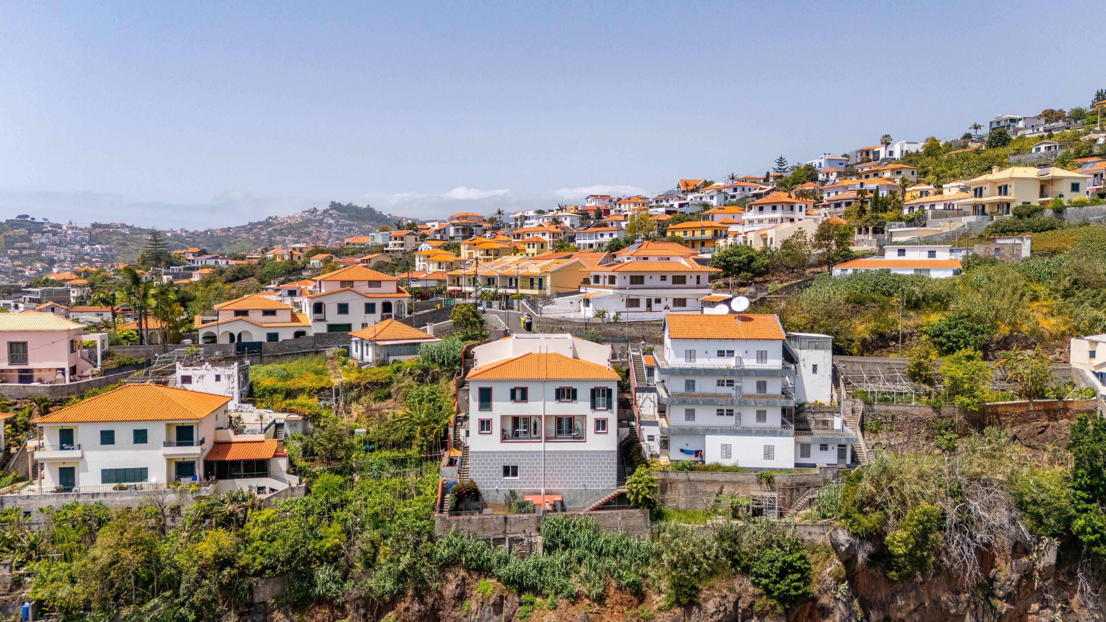 A hillside residential area with terraced houses, some with balconies, and a clear sky.