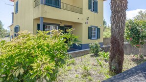 A two-story building with a balcony, surrounded by greenery and a tree. - L&P Countryside by YOUR KEY (Santana)