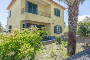 A two-story building with a balcony, surrounded by greenery and a tree. - L&P Countryside by YOUR KEY (Santana)