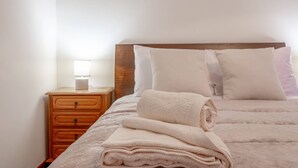 A neatly made bed with a folded blanket and pillows, a wooden nightstand with a lamp, and a wall-mounted light. - L&P Countryside by YOUR KEY (Santana)