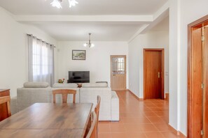 A living room with a sofa set, a dining table, a TV, and a door. - L&P Countryside by YOUR KEY (Santana)
