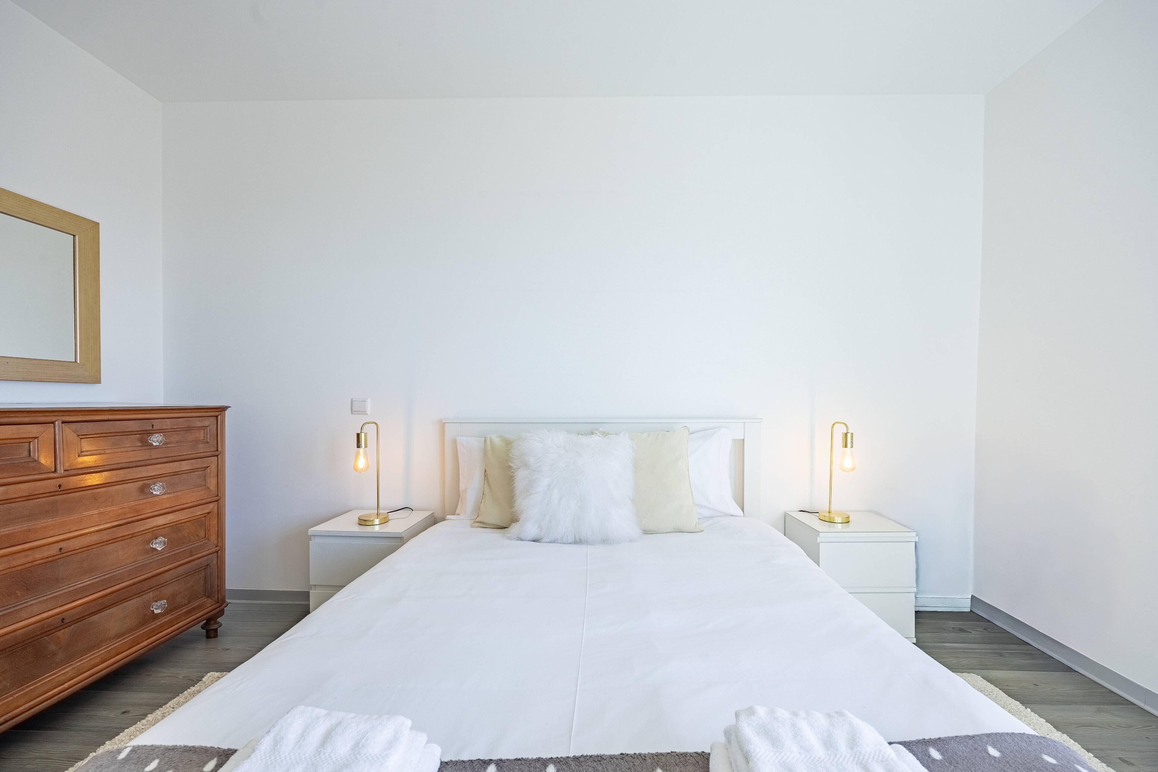 Un dormitorio con una cama grande, dos mesitas de noche, un aparador de madera y un espejo en la pared.