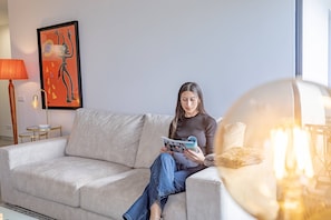 A person sitting on a sofa in a room with a lamp, a framed artwork, and a table with a lamp. - Lux Mare Funchal by YOUR KEY (Funchal)