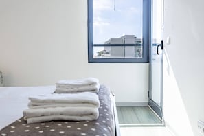 A hotel room with a bed, a window with a view of buildings, and a door. - Lux Mare Funchal by YOUR KEY (Funchal)
