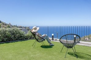Una persona descansando en una silla en un área verde con vista al mar.