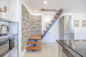 Una cocina moderna con un detalle de pared de piedra, un refrigerador de acero inoxidable y una escalera de madera.