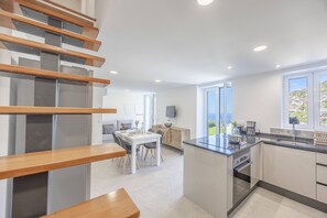 Una cocina moderna con una isla central, un comedor con mesa y sillas, y una escalera con escalones de madera.
