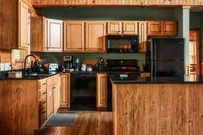 A kitchen with wooden cabinets, a black refrigerator, a microwave, and a dishwasher. - VIEWS! / Hot Tub / Panoramic Mountain View Sauna / Games! (Sevierville)