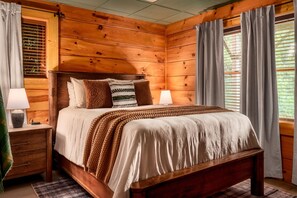 A wooden-paneled bedroom with a bed, two bedside tables, and a window with curtains. - VIEWS! / Hot Tub / Panoramic Mountain View Sauna / Games! (Sevierville)