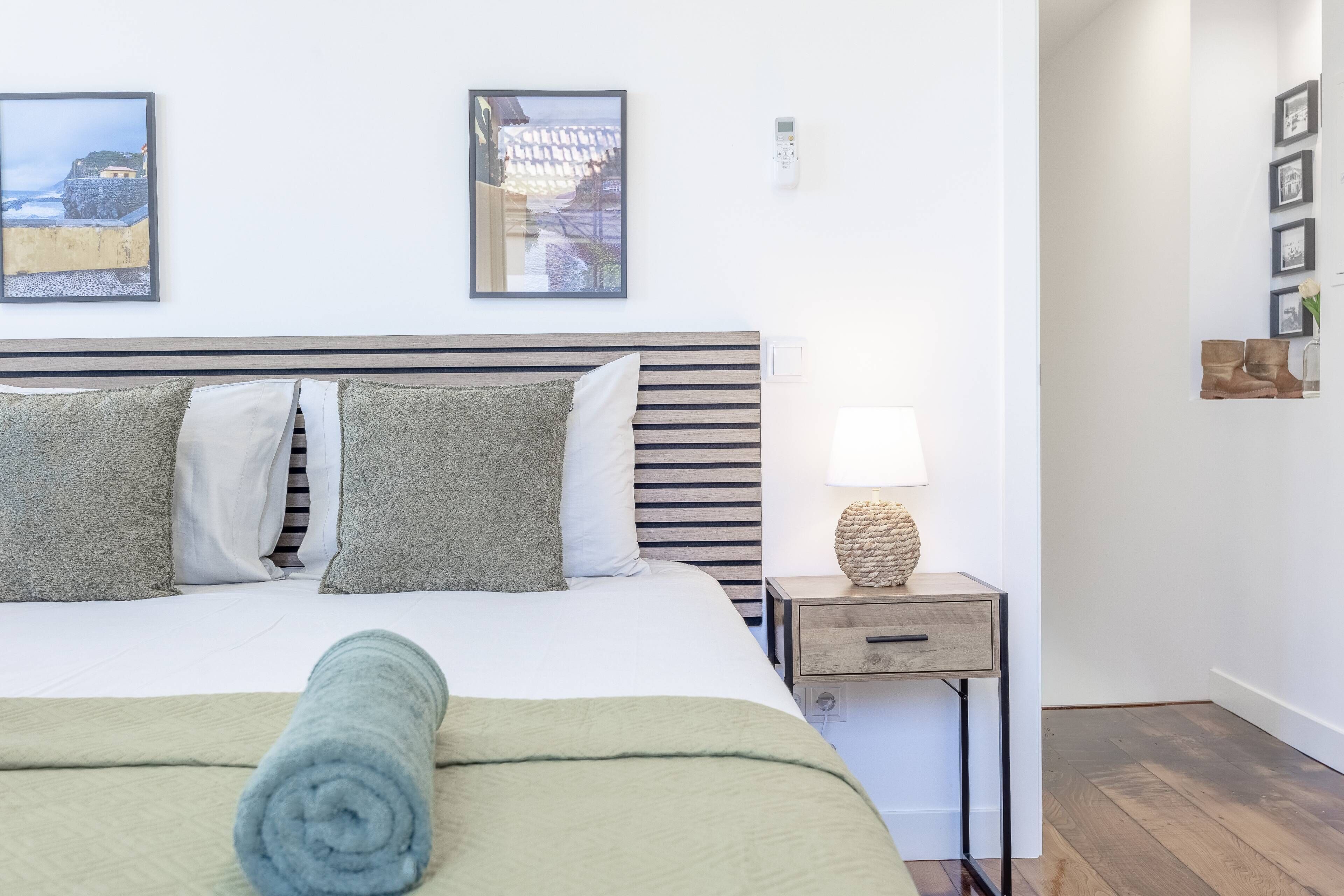 A neatly made bed with a rolled towel, a bedside table with a lamp, and framed pictures on the wall.