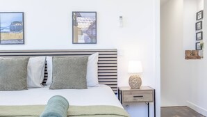 A neatly made bed with a rolled towel, a bedside table with a lamp, and framed pictures on the wall. - Maison Des Souvenir B by YOUR KEY (Ribeira Brava)