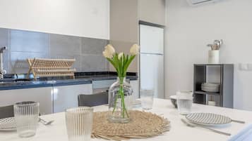 Une cuisine moderne avec une table à manger dressée pour quatre personnes, agrémentée de verres transparents, d’un set de table en fibres naturelles et d’un vase avec des fleurs blanches.
