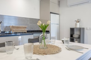 Cocina moderna con una mesa de comedor lista para cuatro personas, que incluye cristalería transparente, un mantel tejido y un florero con flores blancas.